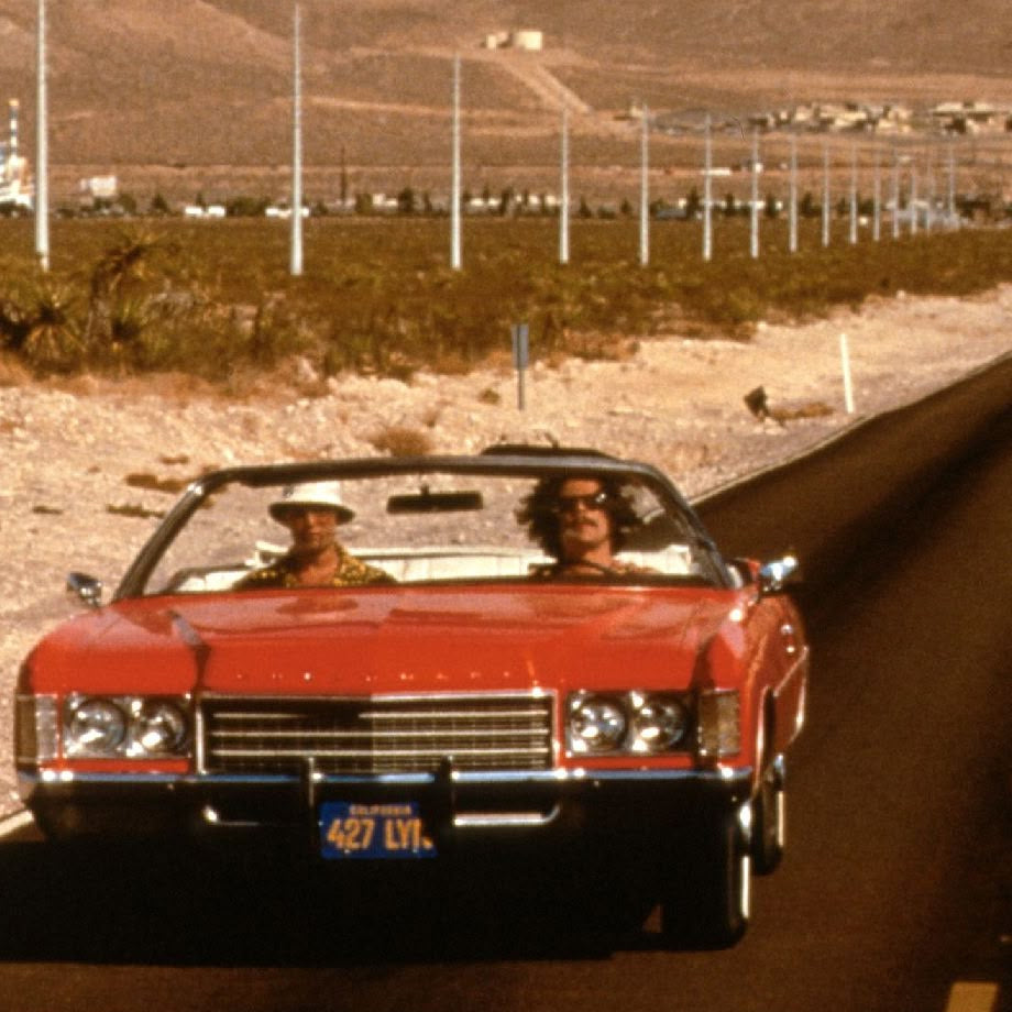 Red convertible car on a desert highway with mountains in the background