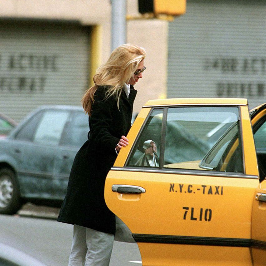 Woman getting into a yellow taxi in New York City with a 'Manhattan Bridge' sign in the background.