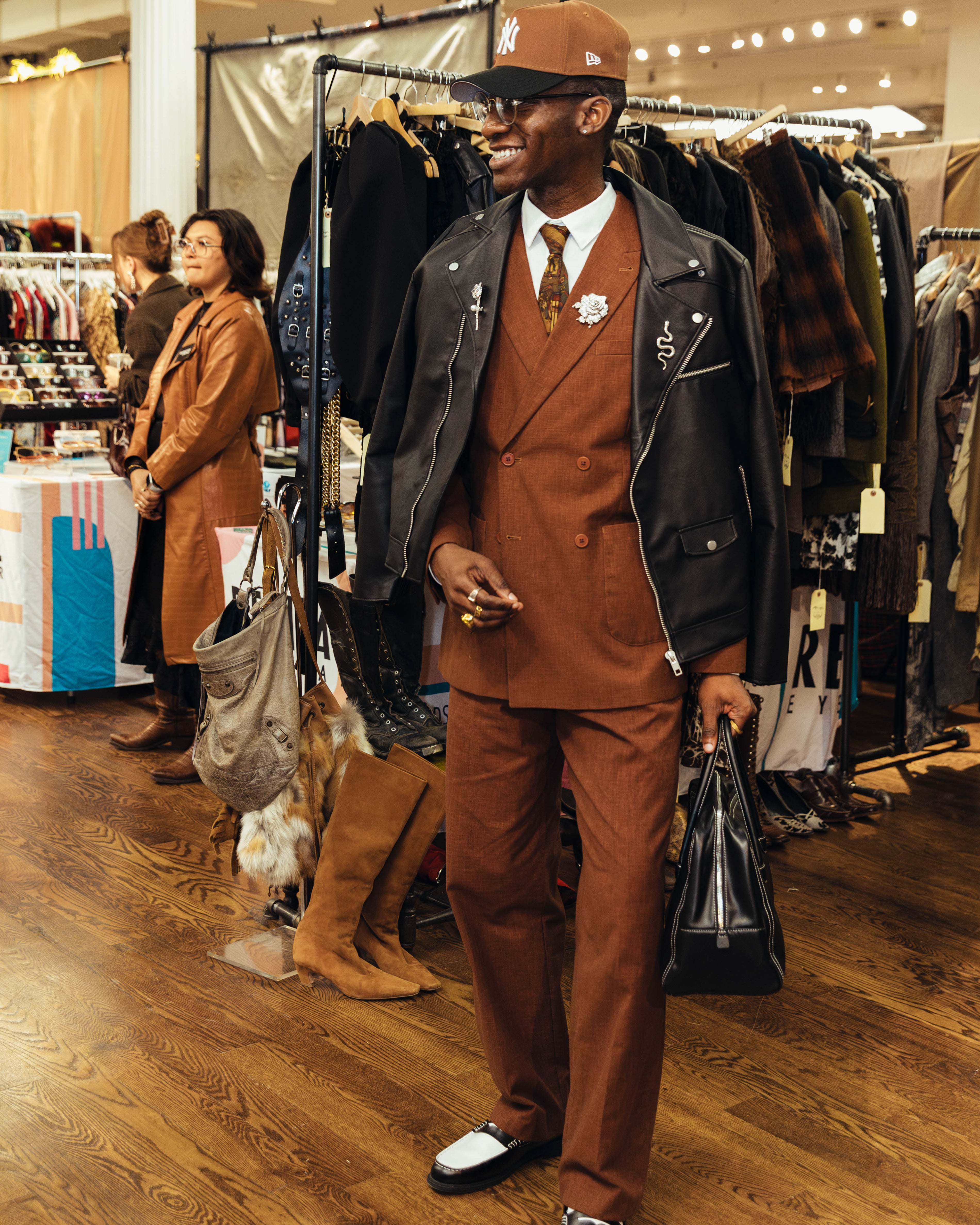 Man in a brown suit and cap walking through a clothing store.