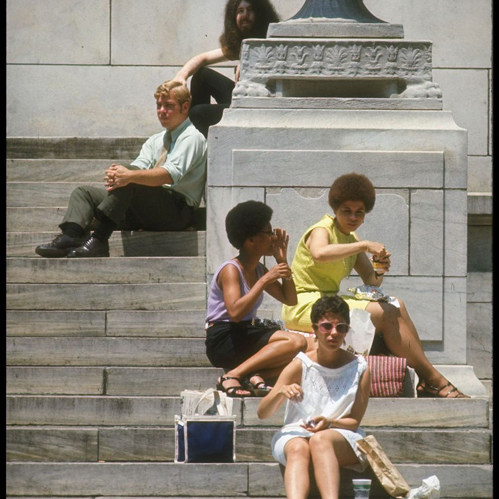 People sitting on stone steps in front of a classical building